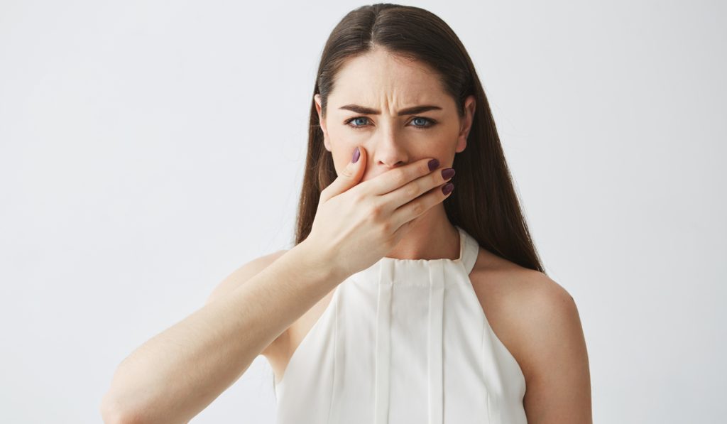 Displeased young brunette girl covering mouth with hand looking at camera over white backround.