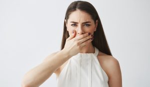 Displeased young brunette girl covering mouth with hand looking at camera over white backround.